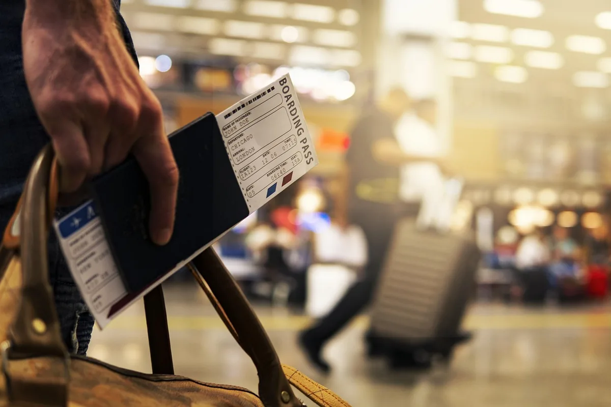 Podróżny trzyma paszport z kartą pokładową i torbę w hali odlotów lotniska