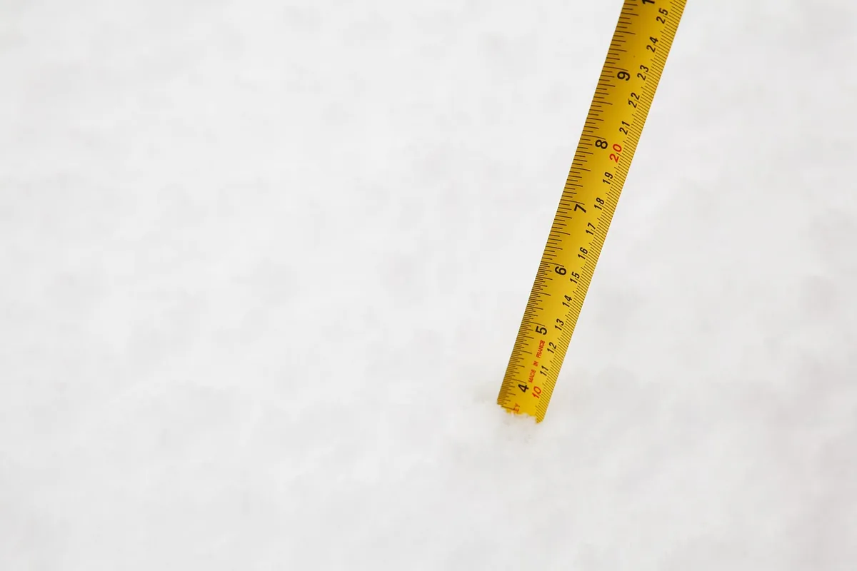 Żółta miarka ze skalą w centymetrach wbita pionowo w świeży, puszysty śnieg