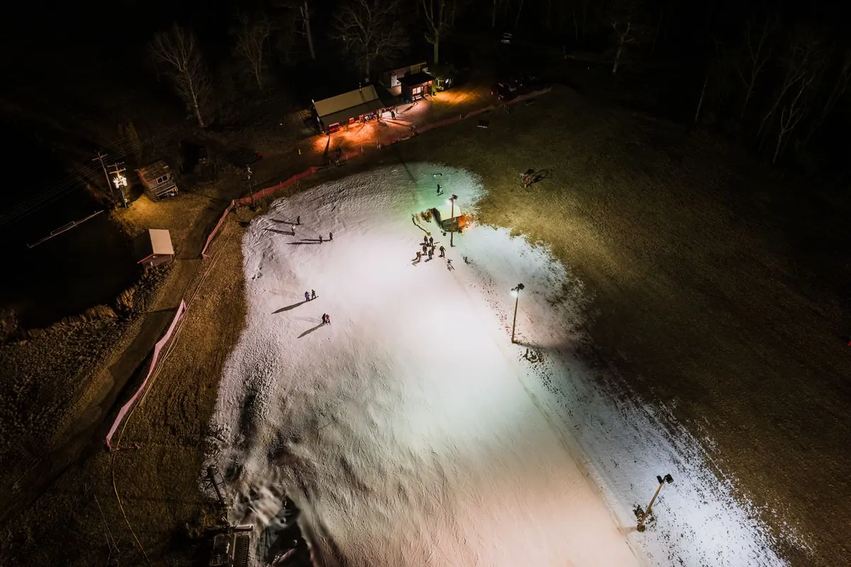 Oświetlony reflektorami stok narciarski nocą wśród ciemnego lasu, widok z lotu ptaka