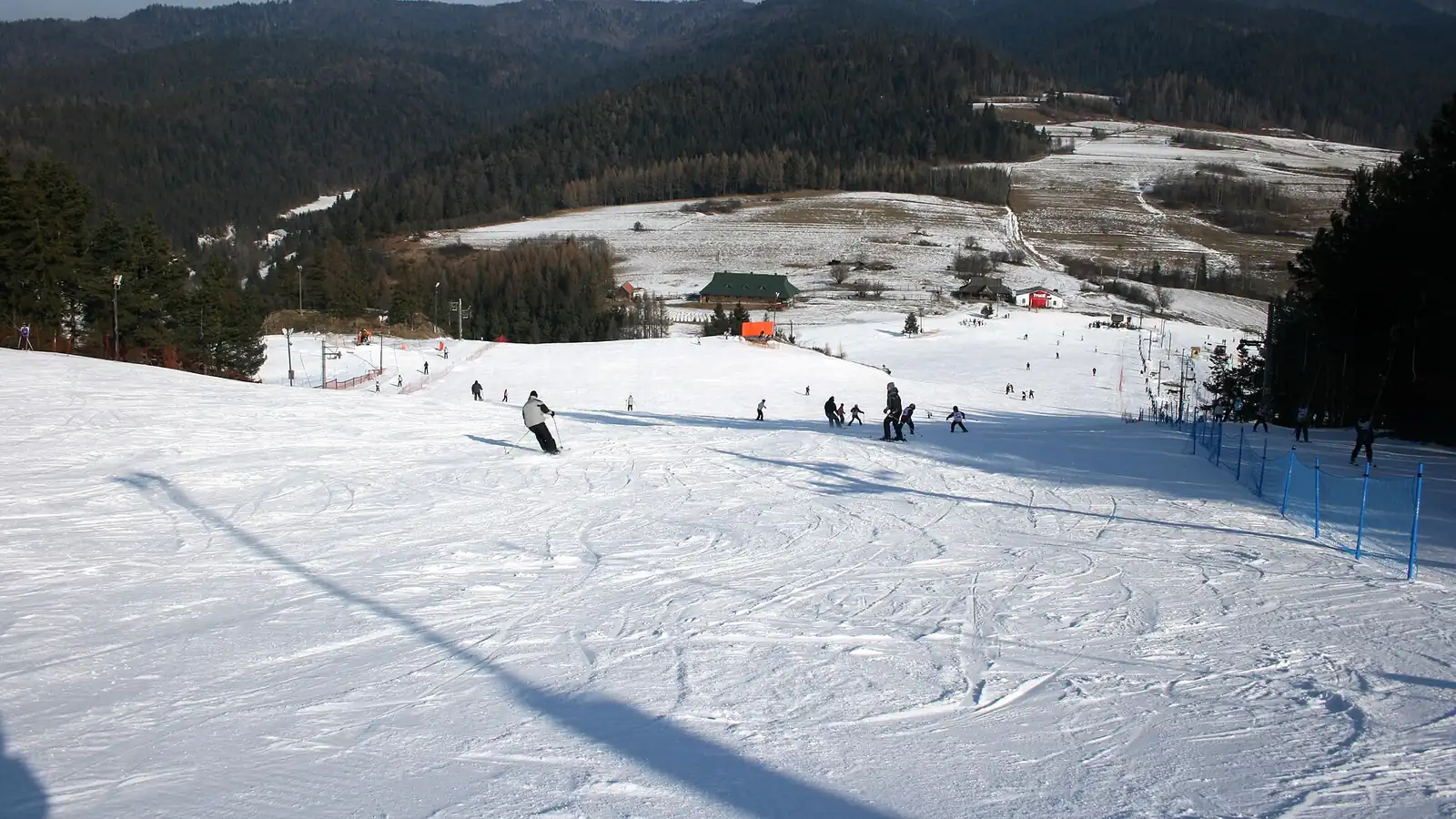 Ośnieżona trasa narciarska Czorsztyn-Ski w Kluszkowcach, w tle zalesione wzgórza i błękitne niebo