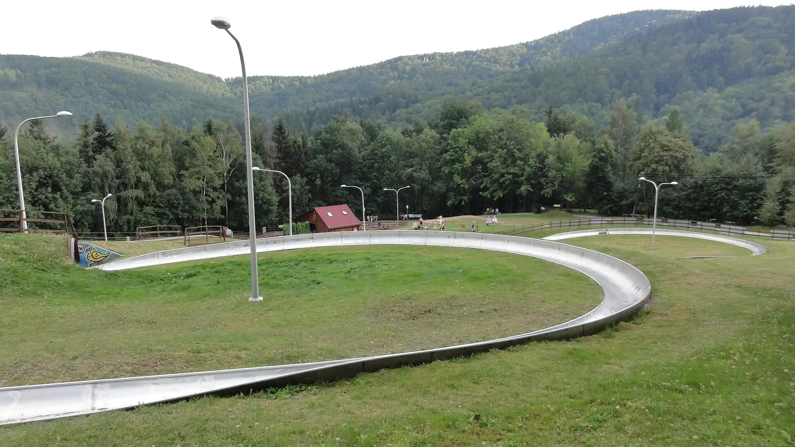 Letni tor saneczkowy i trawiasty stok z latarniami na Dębowcu, w tle zalesione Beskidy
