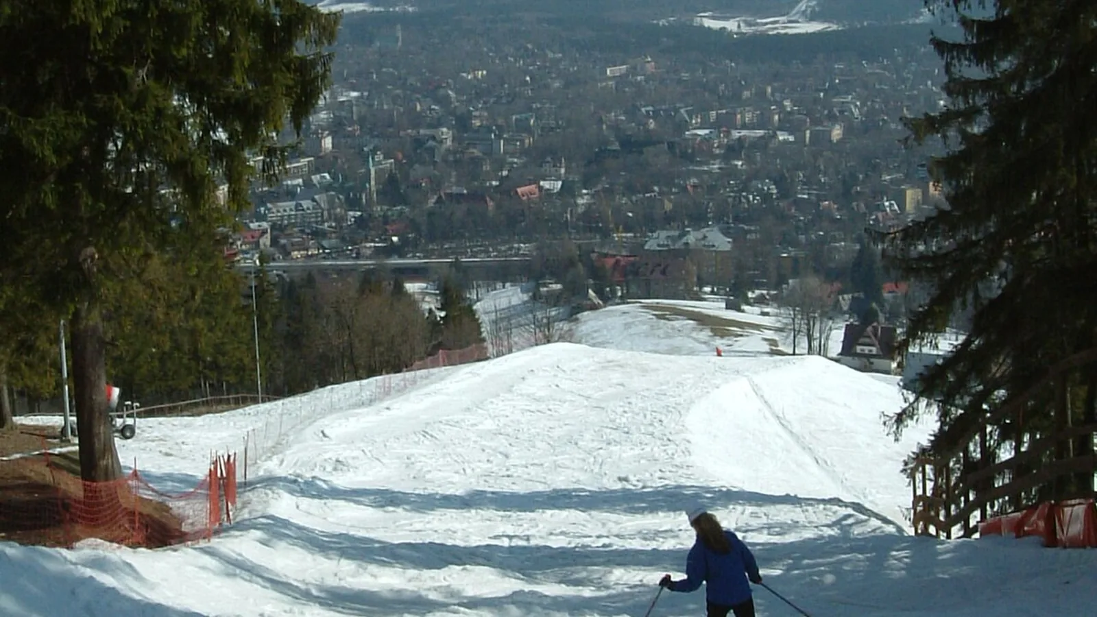 Ośnieżona trasa zjazdowa na Gubałówce między świerkami, w dole Zakopane i Tatry