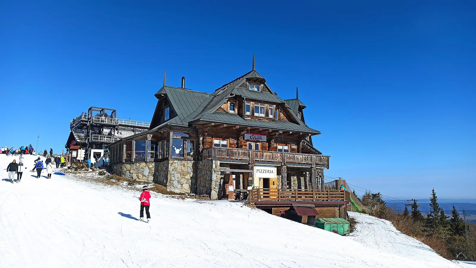 Drewniany budynek restauracji na ośnieżonym szczycie Jaworzyny Krynickiej, narciarze na stoku