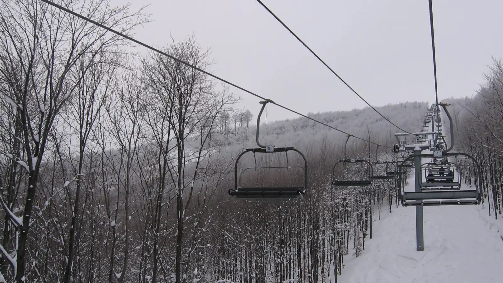 Kolej krzesełkowa biegnąca przez ośnieżony bukowy las na Mosorny Groń, puste krzesełka na linie