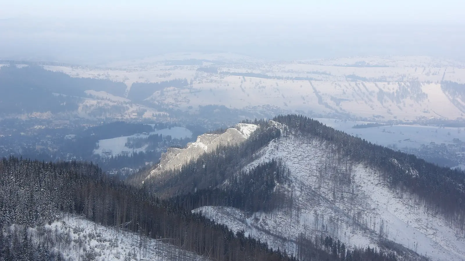 Zalesiony masyw Nosala w śniegu widziany z góry, w tle Zakopane i pagórki Podhala