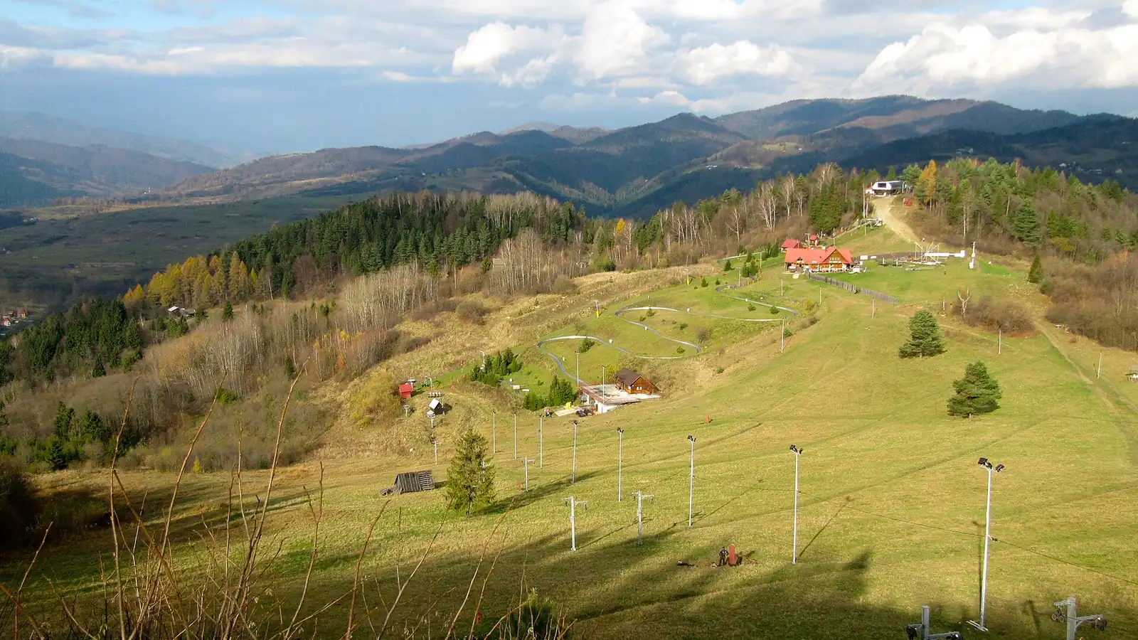 Trawiaste stoki Palenicy z trasami i latarniami, w tle pasma Pienin i Beskidu Sądeckiego jesienią