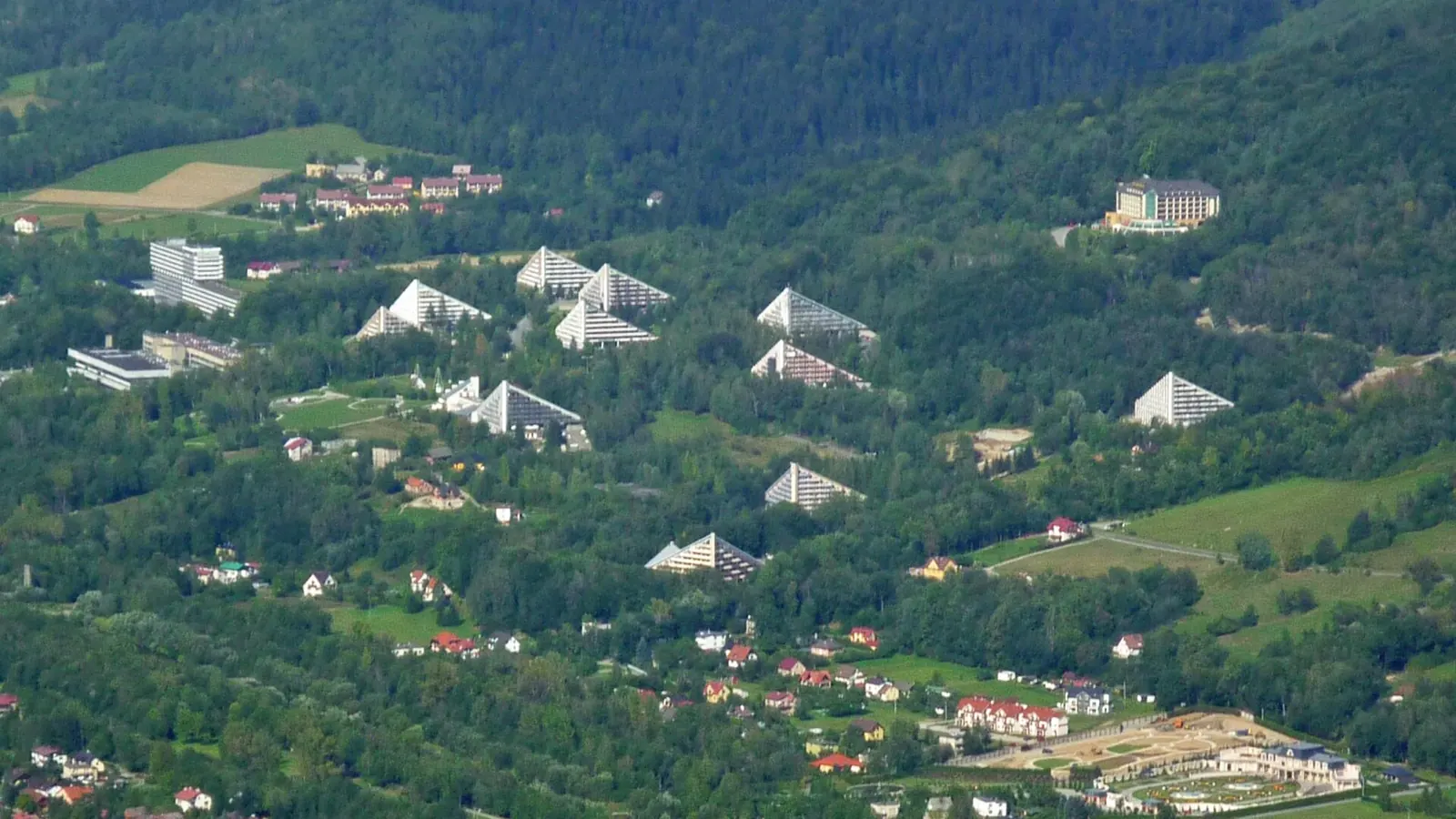Zabudowa Ustronia na zalesionym zboczu z charakterystycznymi hotelami w kształcie piramid, widok z góry latem