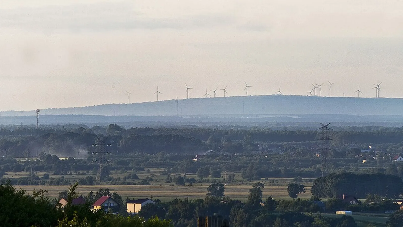 Zalesione wzniesienie Góry Kamieńskiej z wiatrakami na horyzoncie, widok z daleka nad równiną