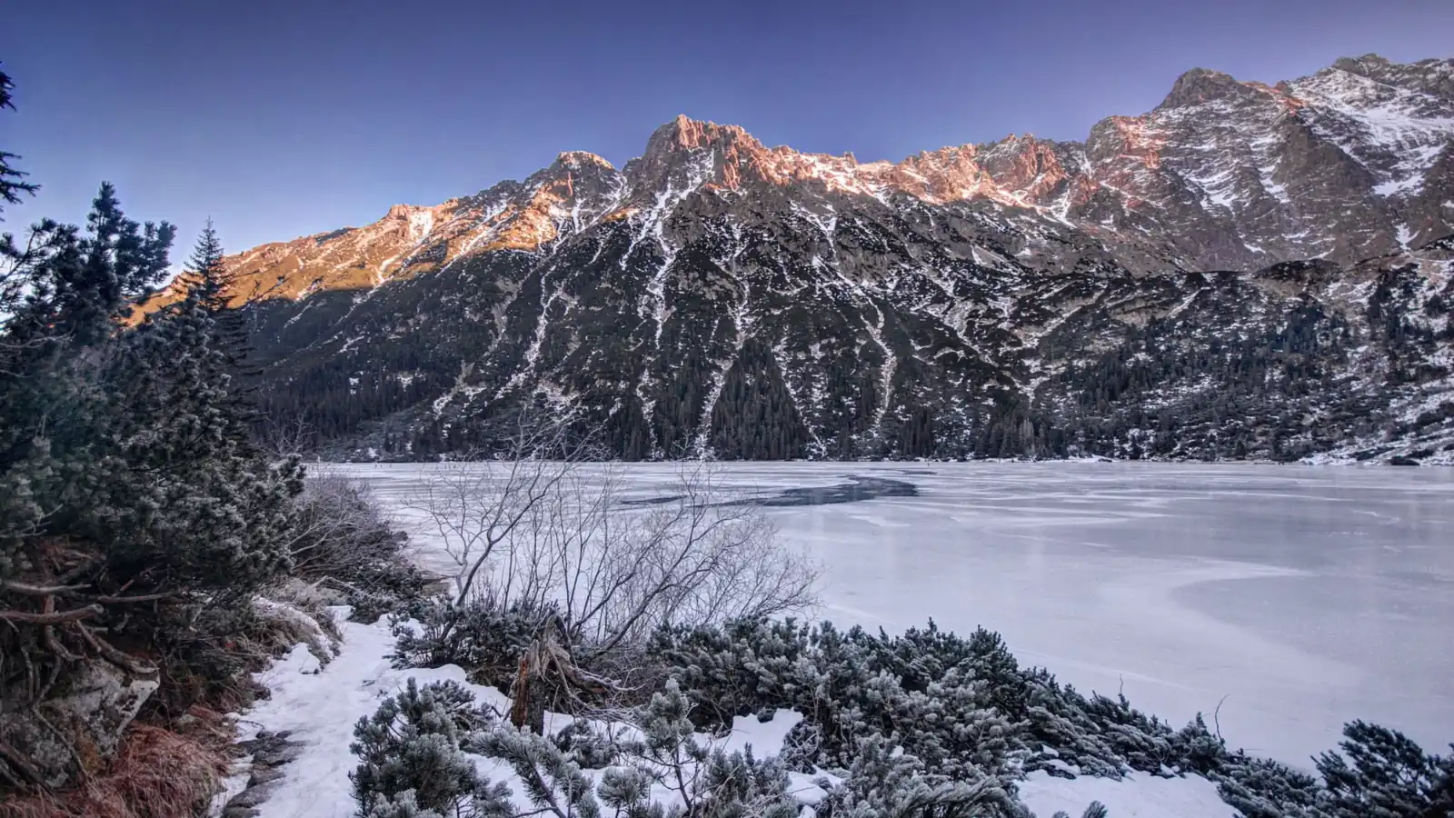 Zamarznięte Morskie Oko i ośnieżone szczyty Tatr oświetlone wieczornym słońcem