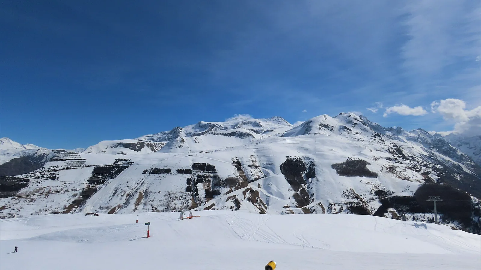 Ośnieżone stoki i wyciągi ośrodka Les Deux Alpes widziane z Le Mais, w tle zaśnieżone szczyty pod błękitnym niebem