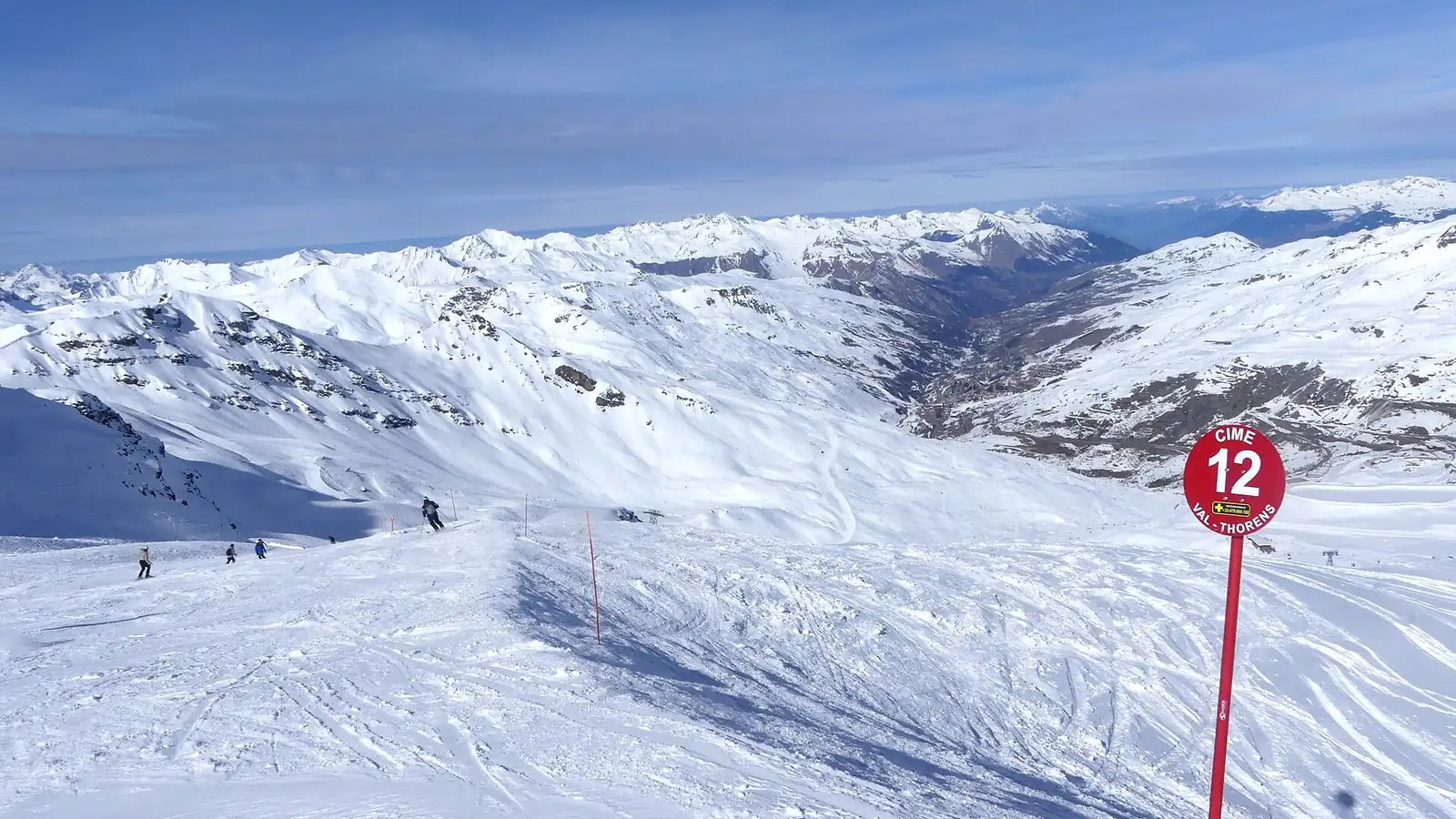 Czerwona trasa narciarska z oznaczeniem numeru biegnąca szerokim grzbietem, w tle ośnieżone Alpy